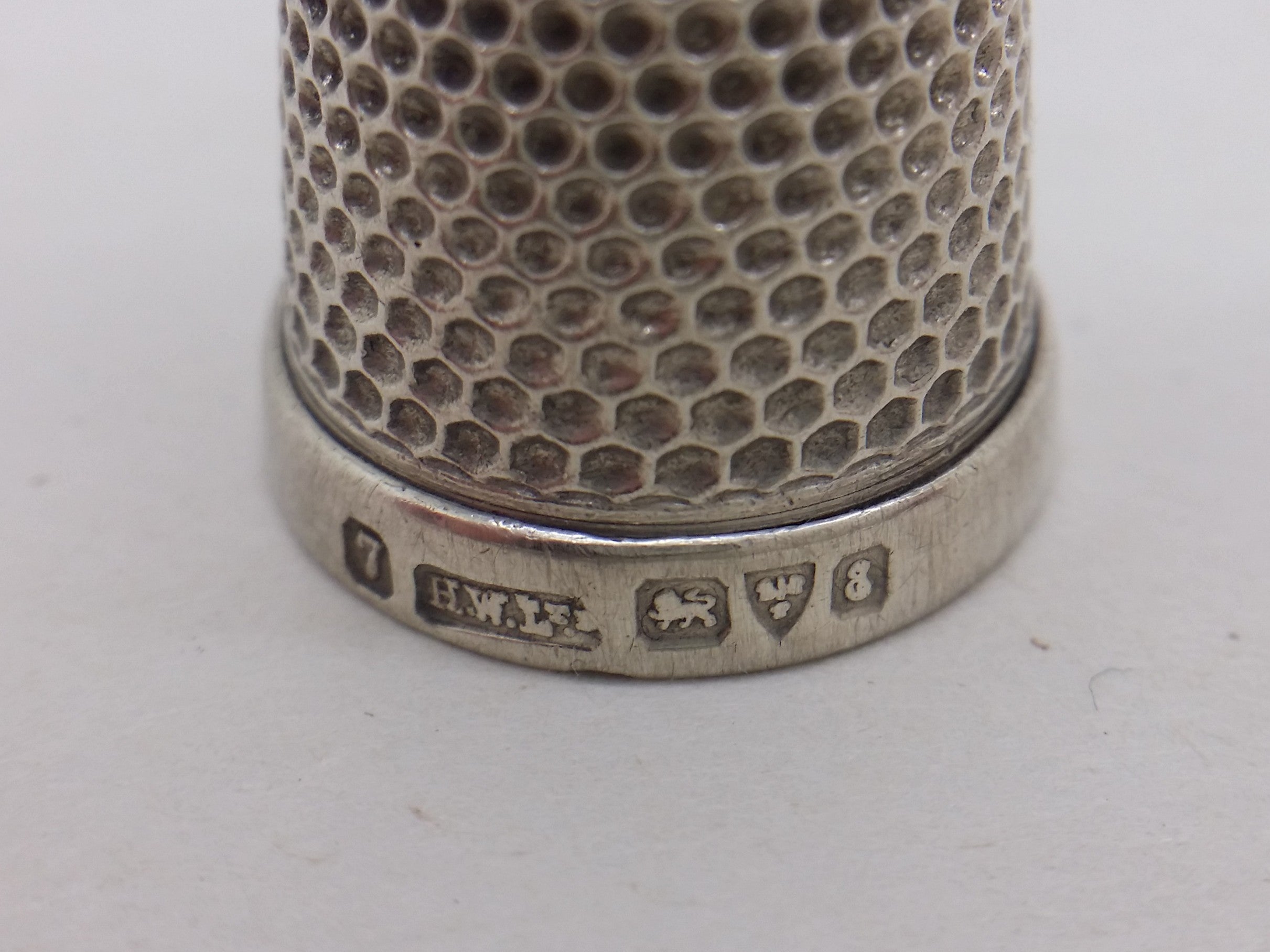 Thimble hallmarks: Size 7 mark; Henry Williamson Ltd maker's mark HWLTD; lion passant mark for sterling silver; three-wheat-sheaves-and-a-sword mark for Chester; and Chester date letter E for 1905.