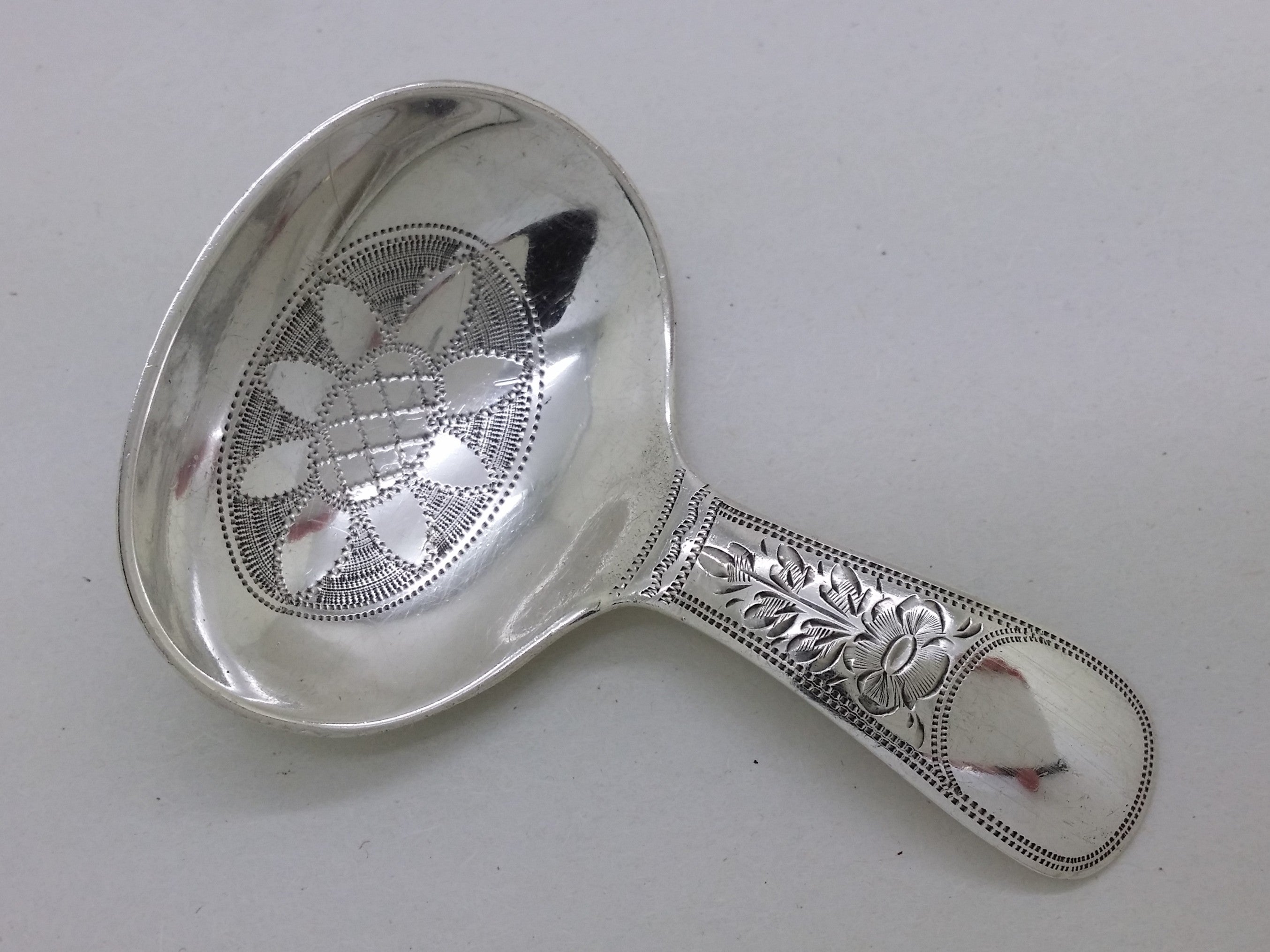 Sterling silver caddy spoon with floral engraved tab handle with a vacant cartouche, and stippled edging.