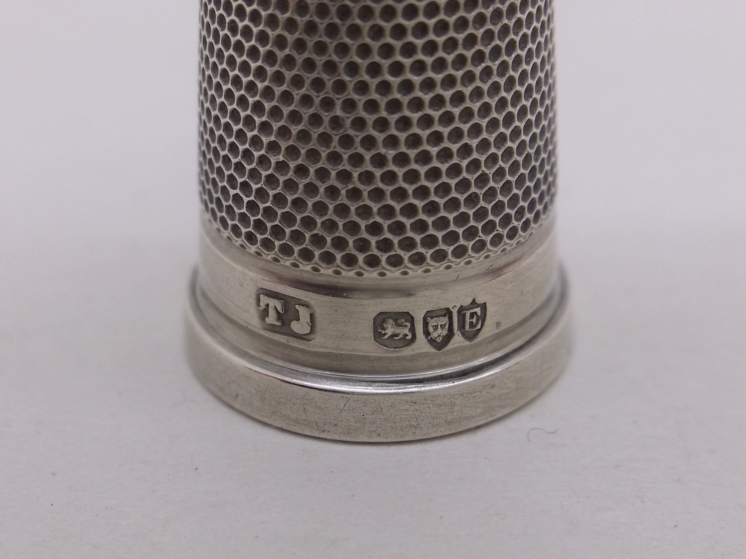 Thimble hallmarks: Johnson, Sons & Edmunds maker's mark TJ for Thomas Johnson; lion passant mark for sterling silver; leopard head mark for London; and London date letter E for 1880.