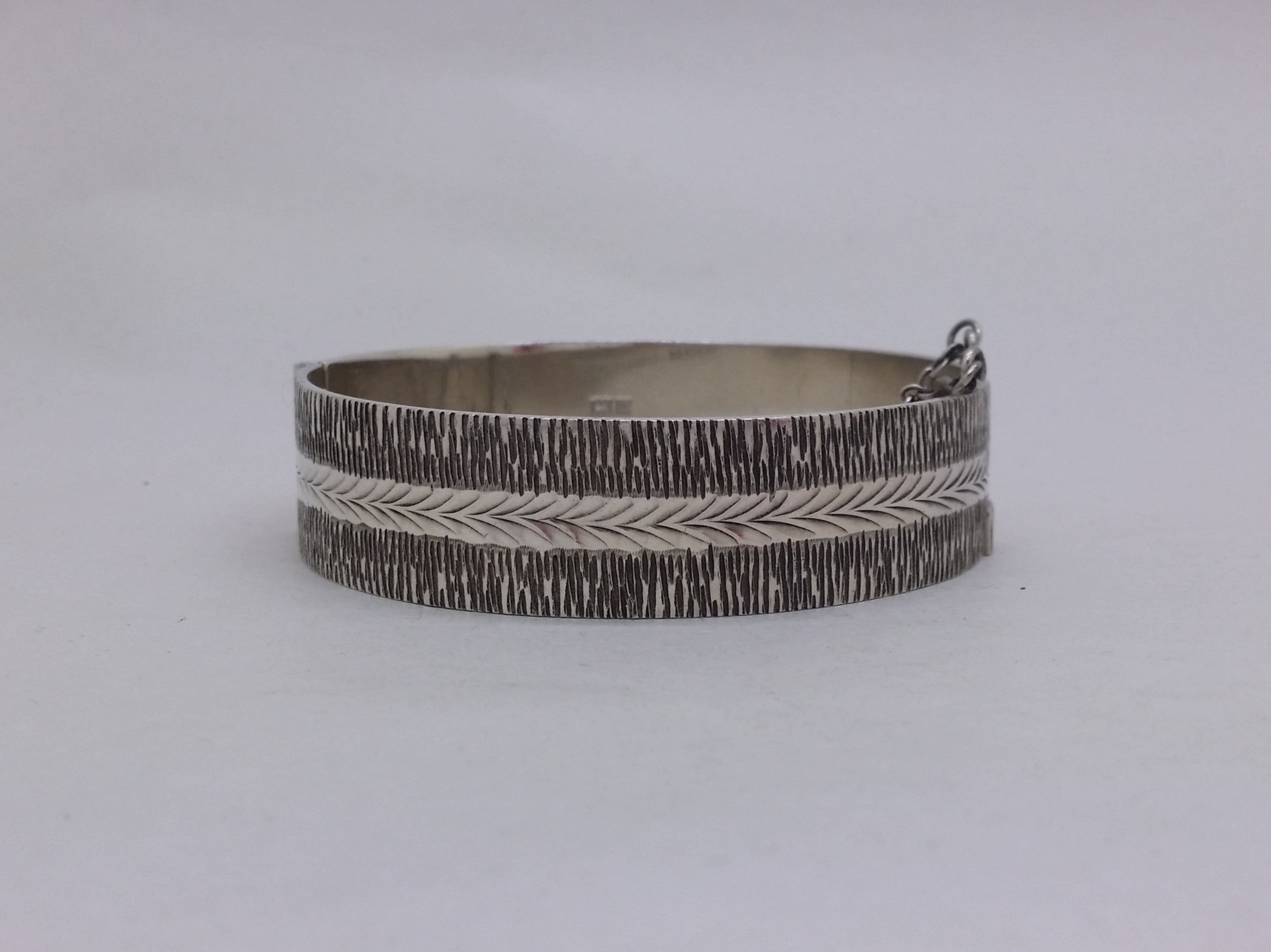 Bright cut herringbone design with textured bark-effect borders on a sterling silver hinged bangle.